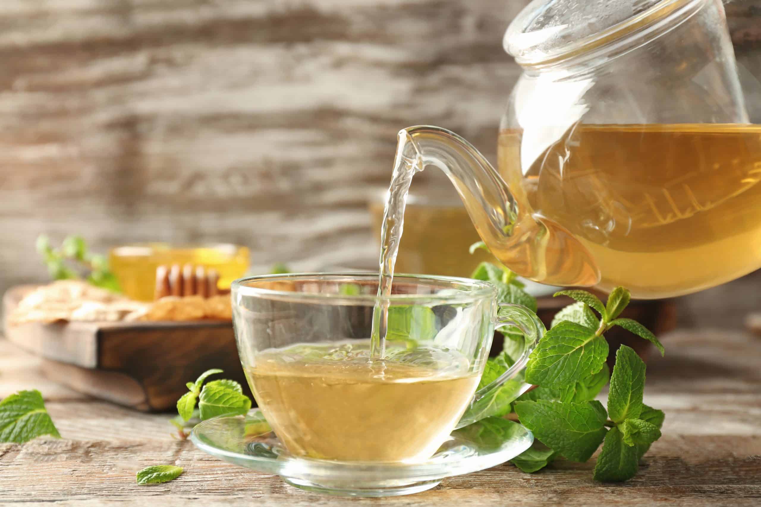 Pouring aromatic lemon balm tea into cup on wooden table