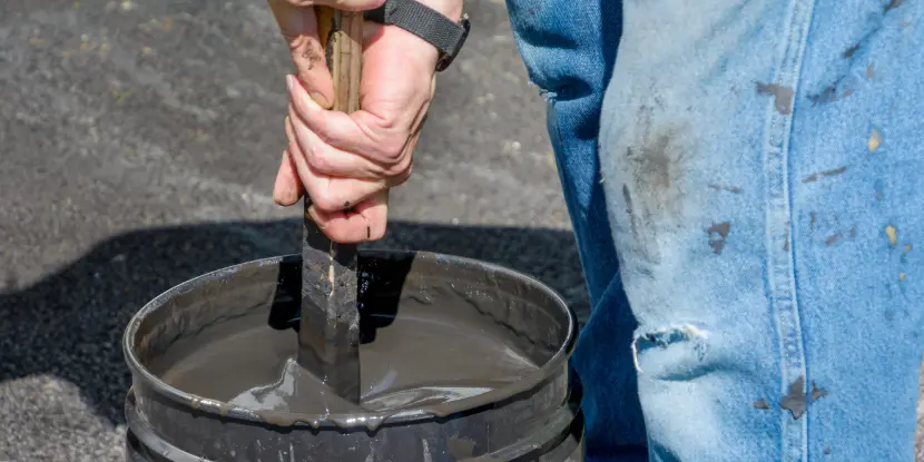 A man stirring a bucket of asphalting material