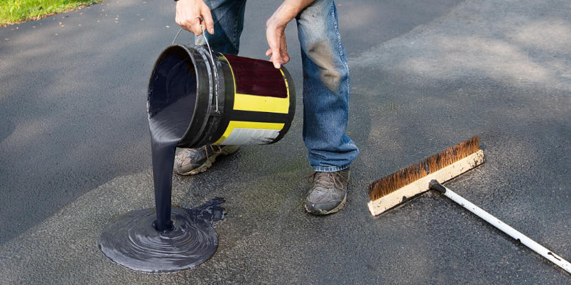 A worker pours sealant onto a driveway