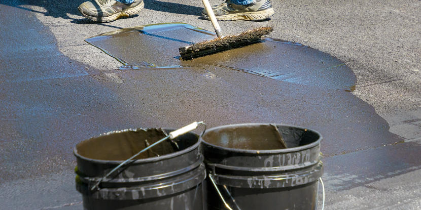 A worker spreads sealant with a bristle brush
