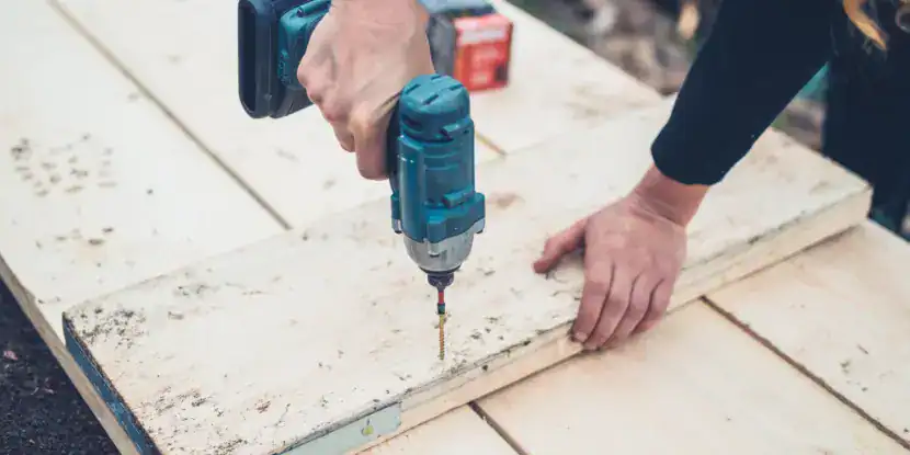A woman uses an impact driver to plant a screw in a heavy board