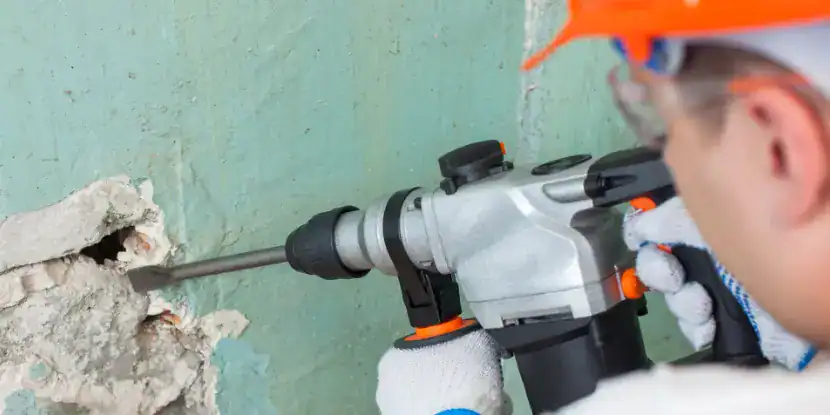 A man uses a power tool to break up a concrete wall